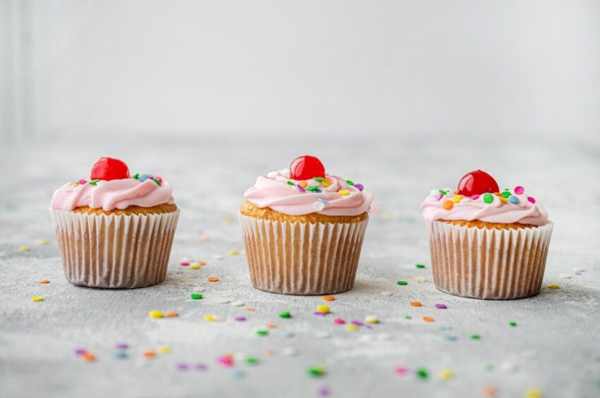 Tre cupcakes med rosa frosting och strössel fotograferade i studio.