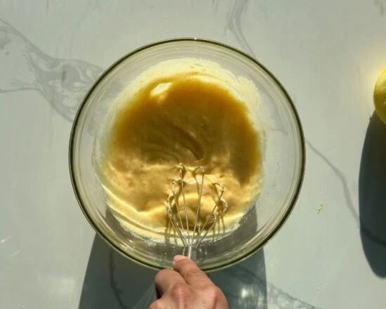 Hand vispar en gul smet i en glasskål på en ljus köksyta